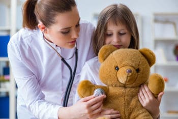 A doctor and small child holding a teddy bear.
