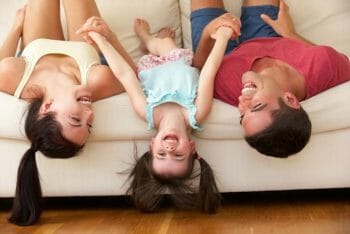 Young couple on couch hanging upside down with their child playing.