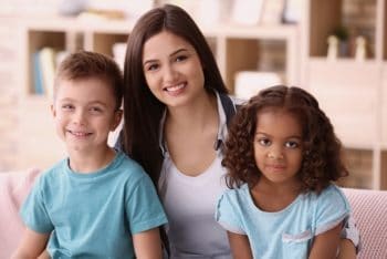 Young lady sitting in between two small children smiling into the camera.