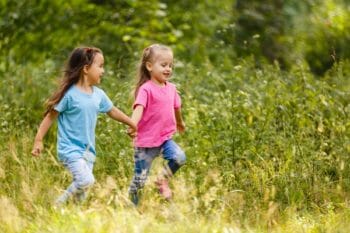 Two young girls holding hands and running.