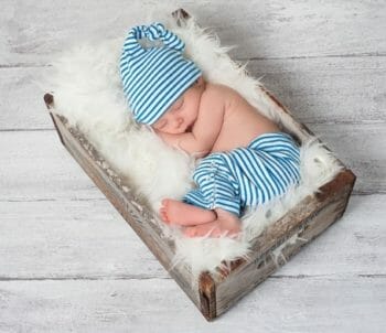Baby posed for a professional photo sleeping in a crate with a fluffy blanket.
