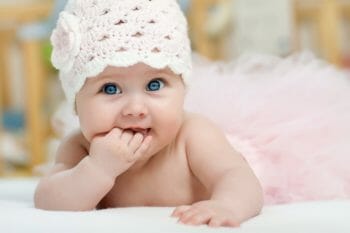Very cute baby looking up at the camera with its fingers in its mouth.