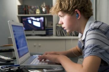 Teen boy wearing earbuds and using the laptop.